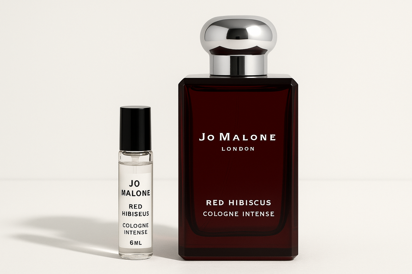 عينة من عطر Jo Malone Red Hibiscus Cologne Intense سعة 6 مل بجوار زجاجة عطر سعة 100 مل من عطر Jo Malone Red Hibiscus Cologne Intense والتي تحتوي على كتابة باللون الأبيض على زجاجة حمراء داكنة
